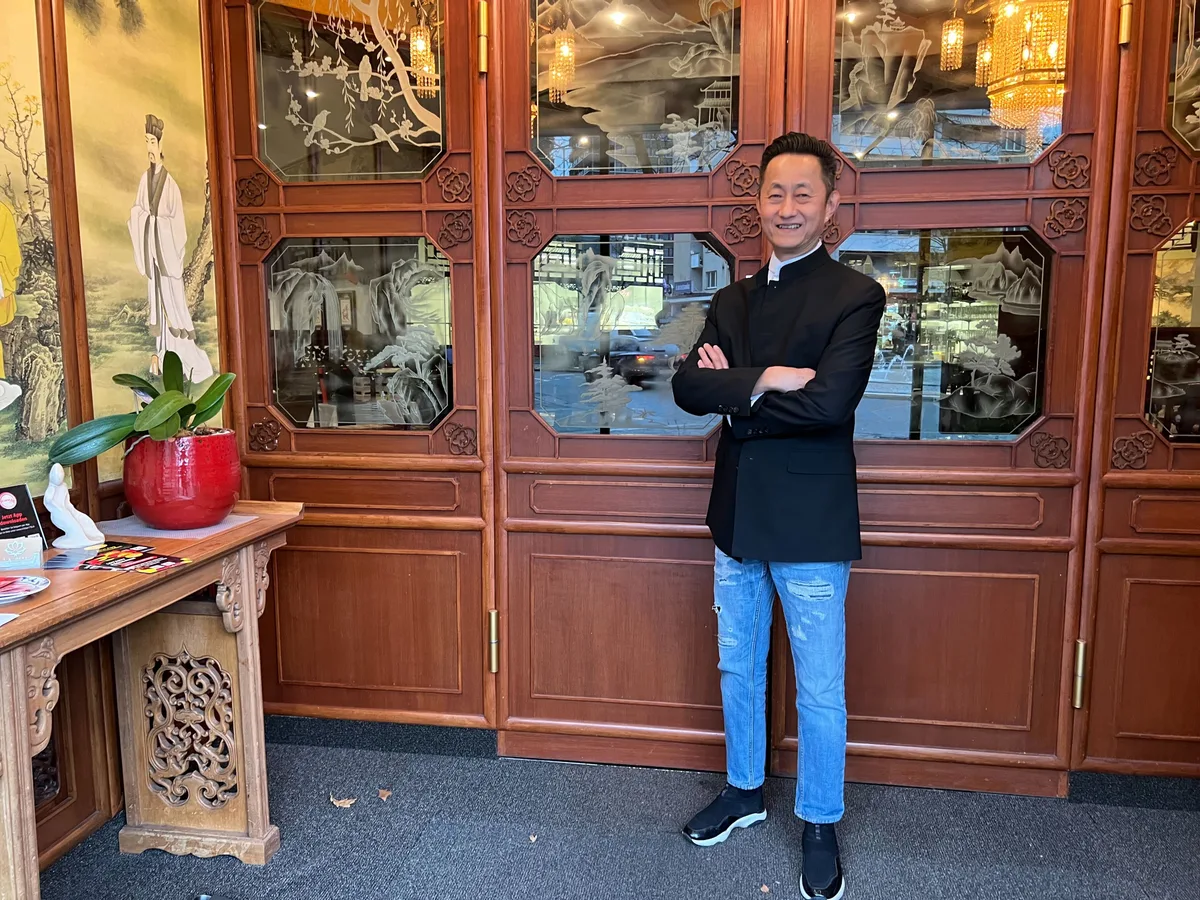Roth Ly, Besitzer der «Suan Long»-Restaurants, steht vor einer Holzwand mit asiatischen Deko-Elementen.